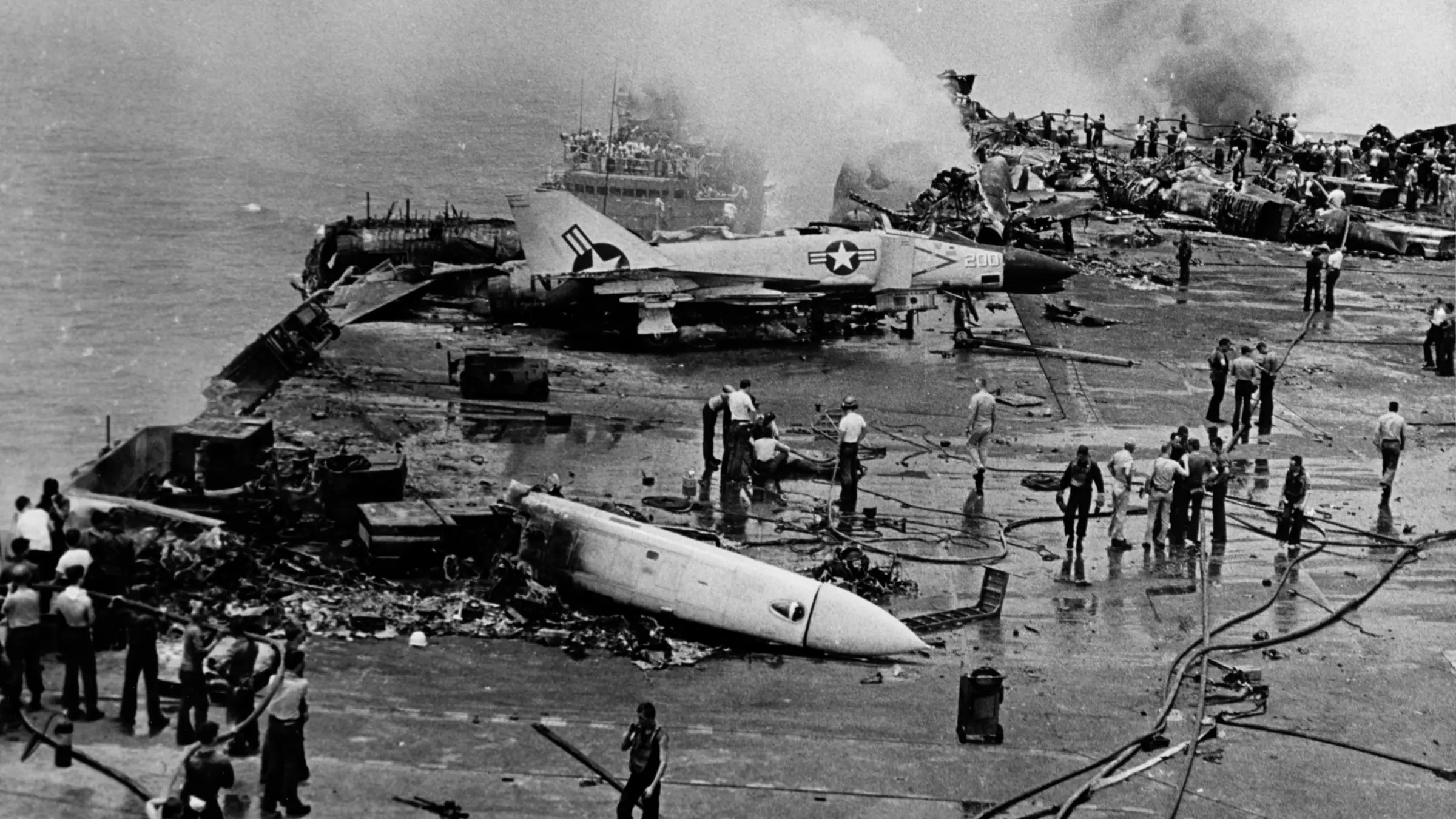 Black-and-white photograph of sailors with hoses on the charred flight deck of USS Forrestal, July 29, 1967.